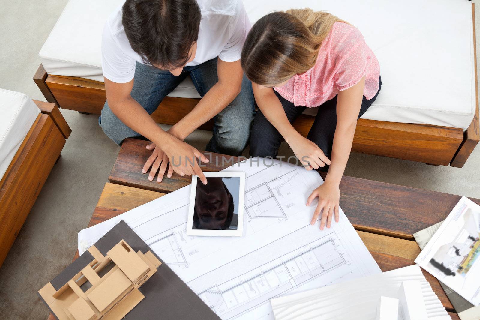 High angle view of couple using tablet PC with blueprint and model structure on table