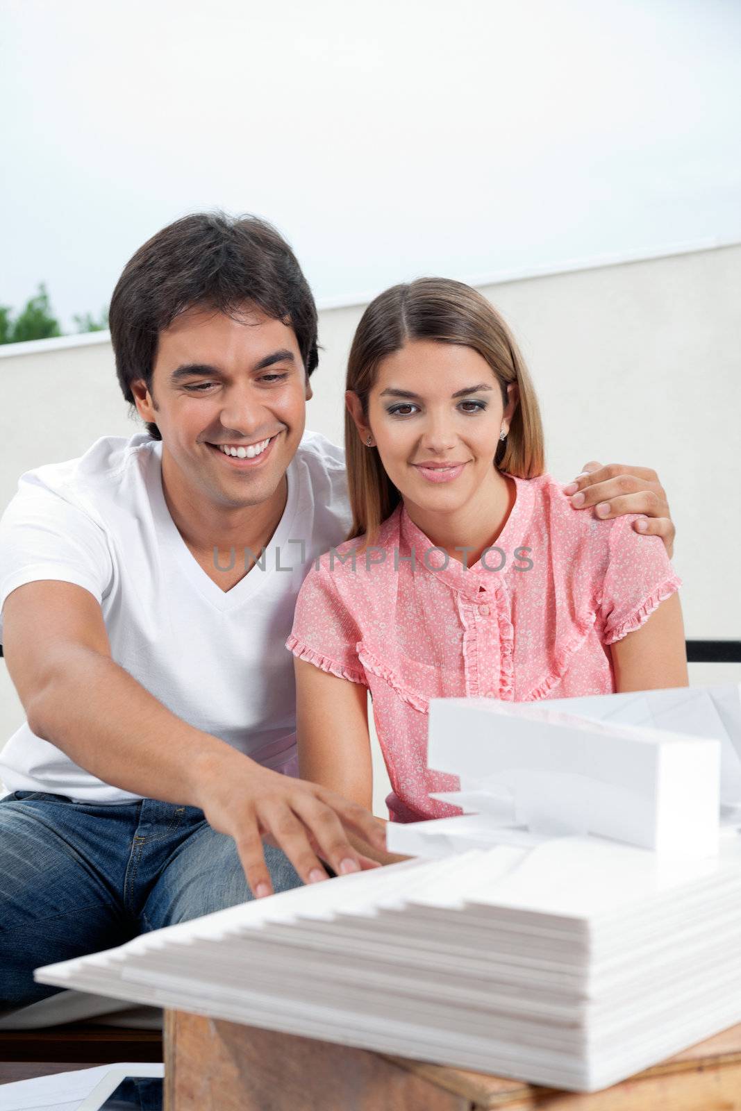 Happy young couple in casuals looking at an architectural model structure