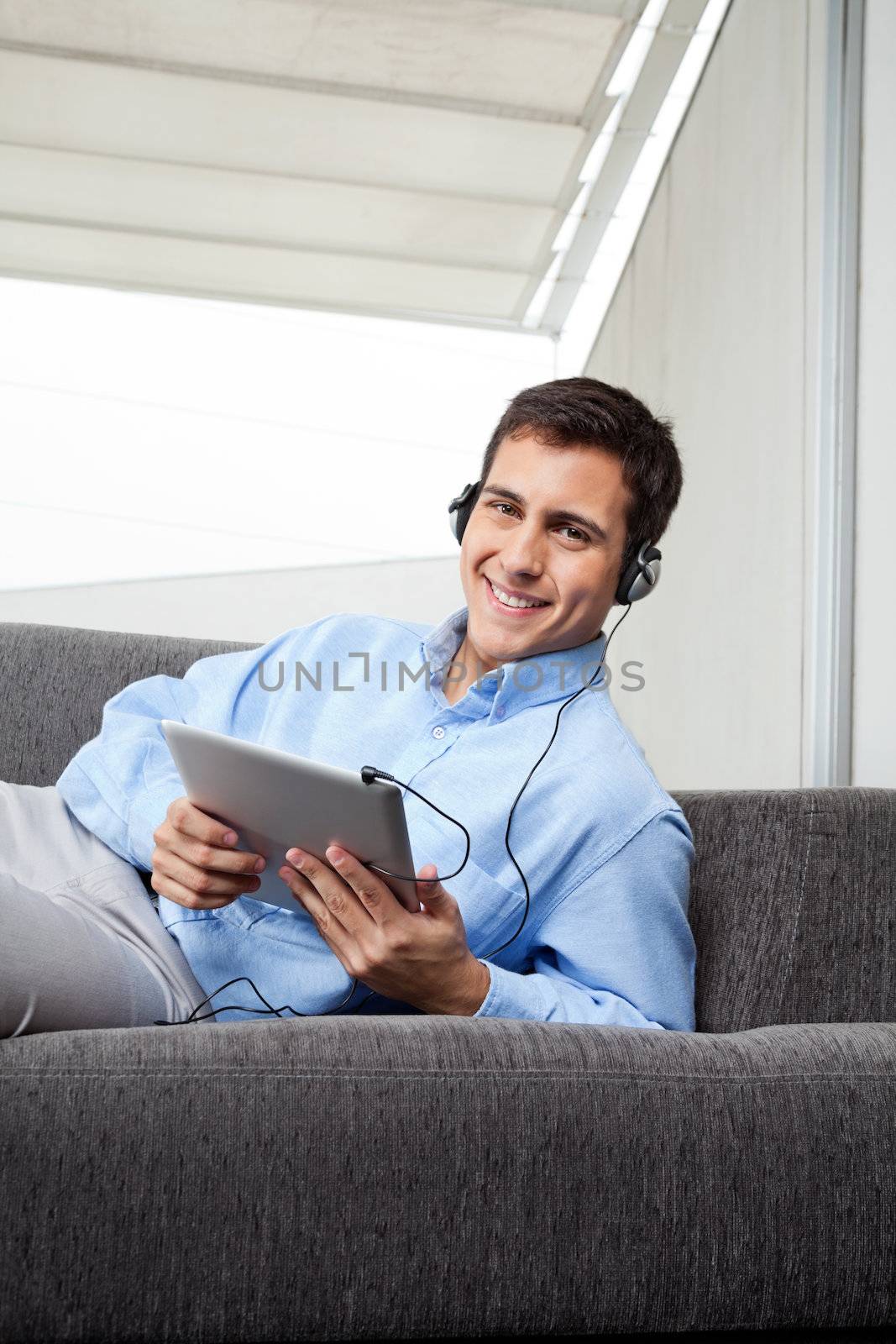 Portrait of happy young man in formal wear listening to music on digital tablet