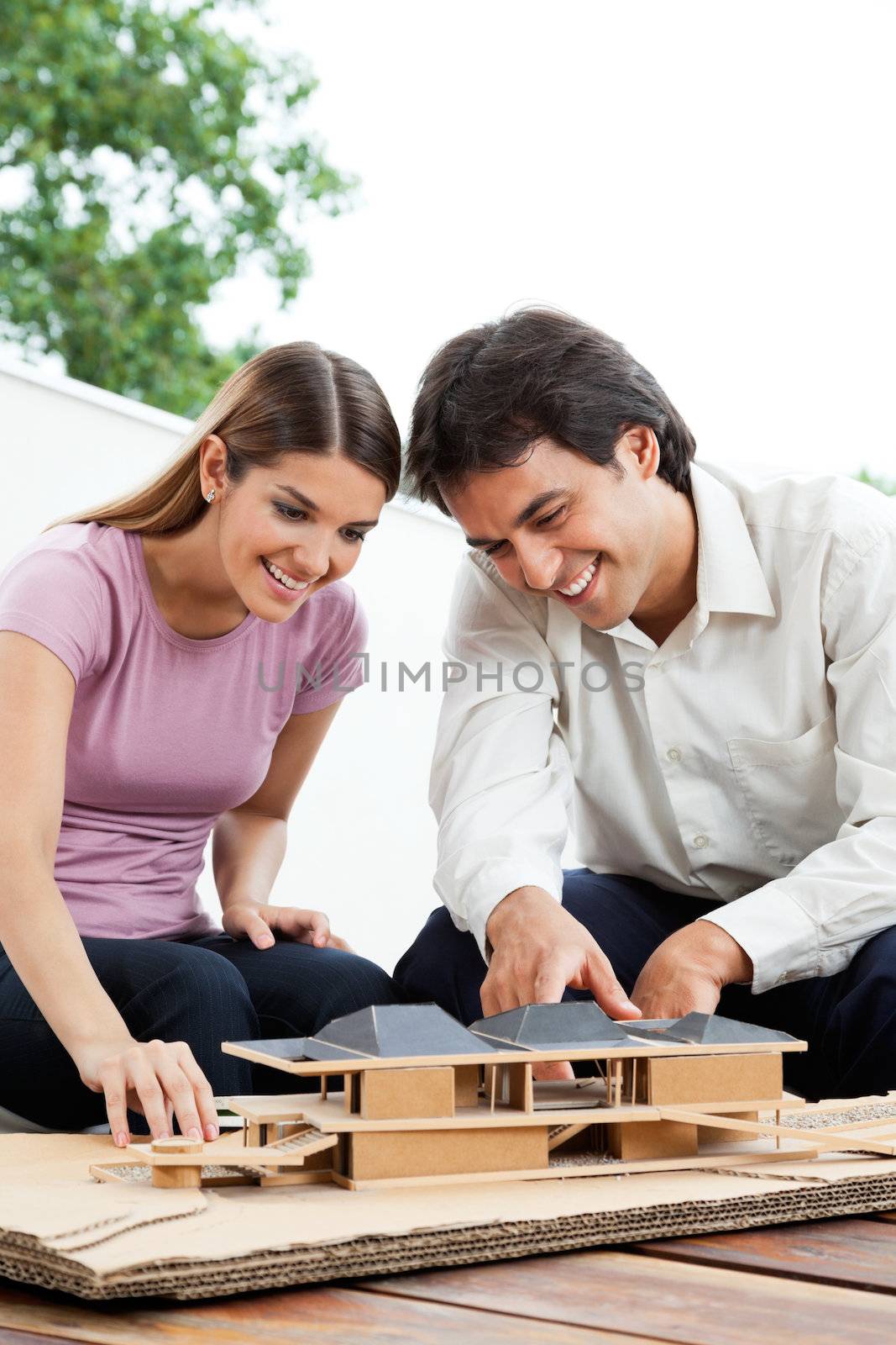 Happy young architects working on a wooden model house together