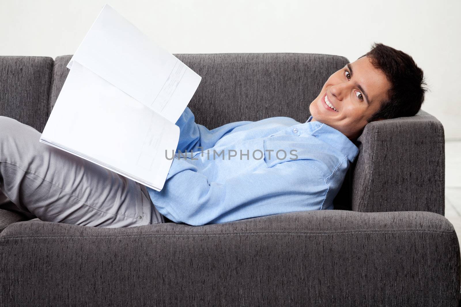 Portrait of young man smiling with magazine while lying on sofa