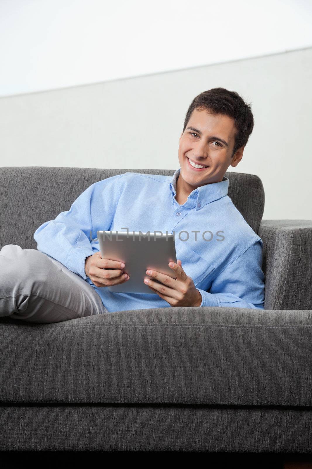 Portrait of happy young man in formal wear holding digital tablet while sitting on sofa