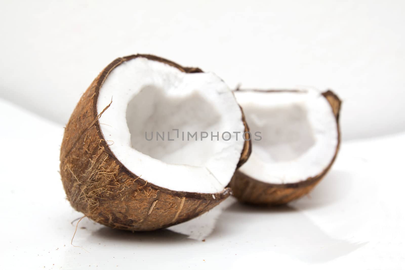 Closeup of cracked coconut on white background with light shadow. Shallow focus depth on front coconut 