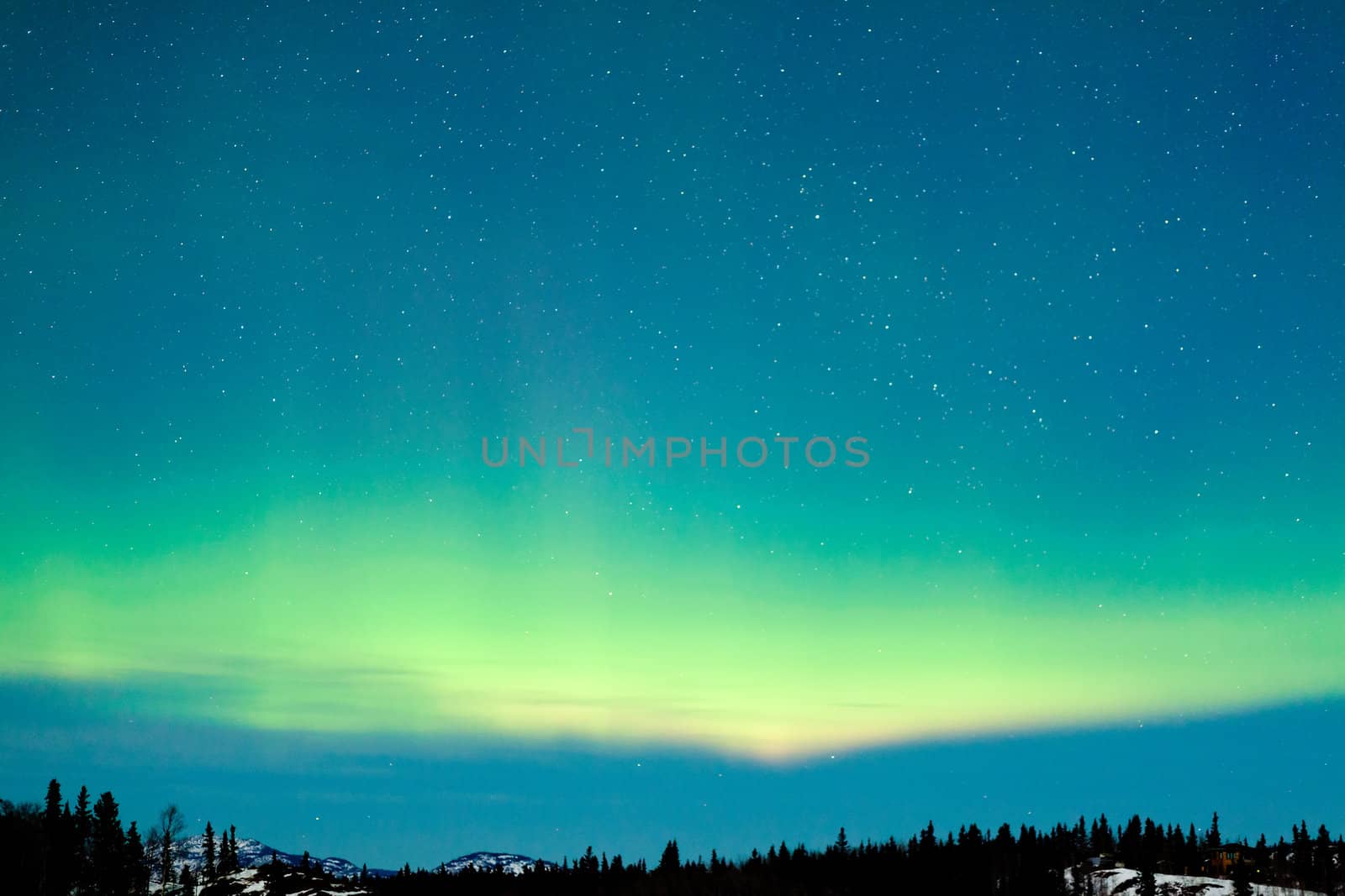 Spectacular display of intense green Northern Lights or Aurora borealis or polar lights over snowy northern winter landscape