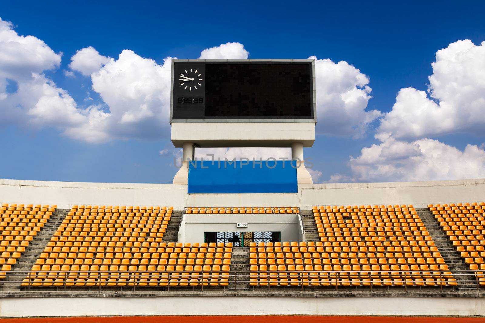 Rows of orange seats on the stadium with scoreboard displaying clock above them