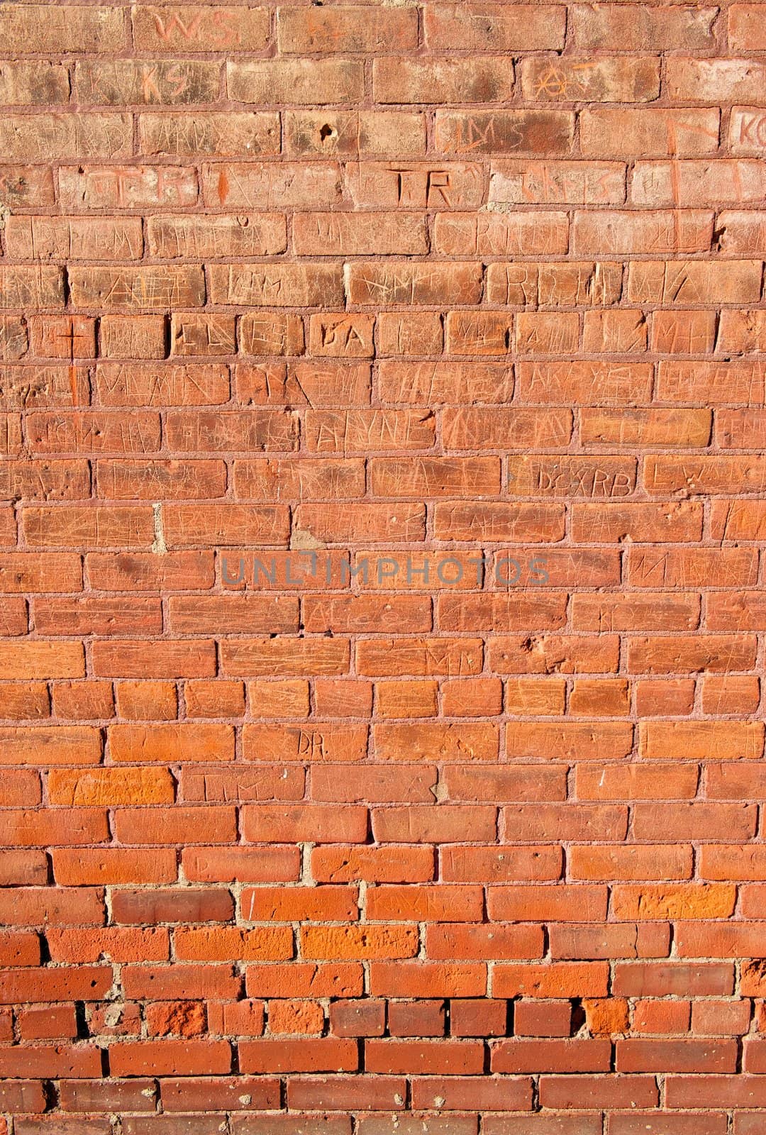 An old, red brick wall that has had many names carved into it.