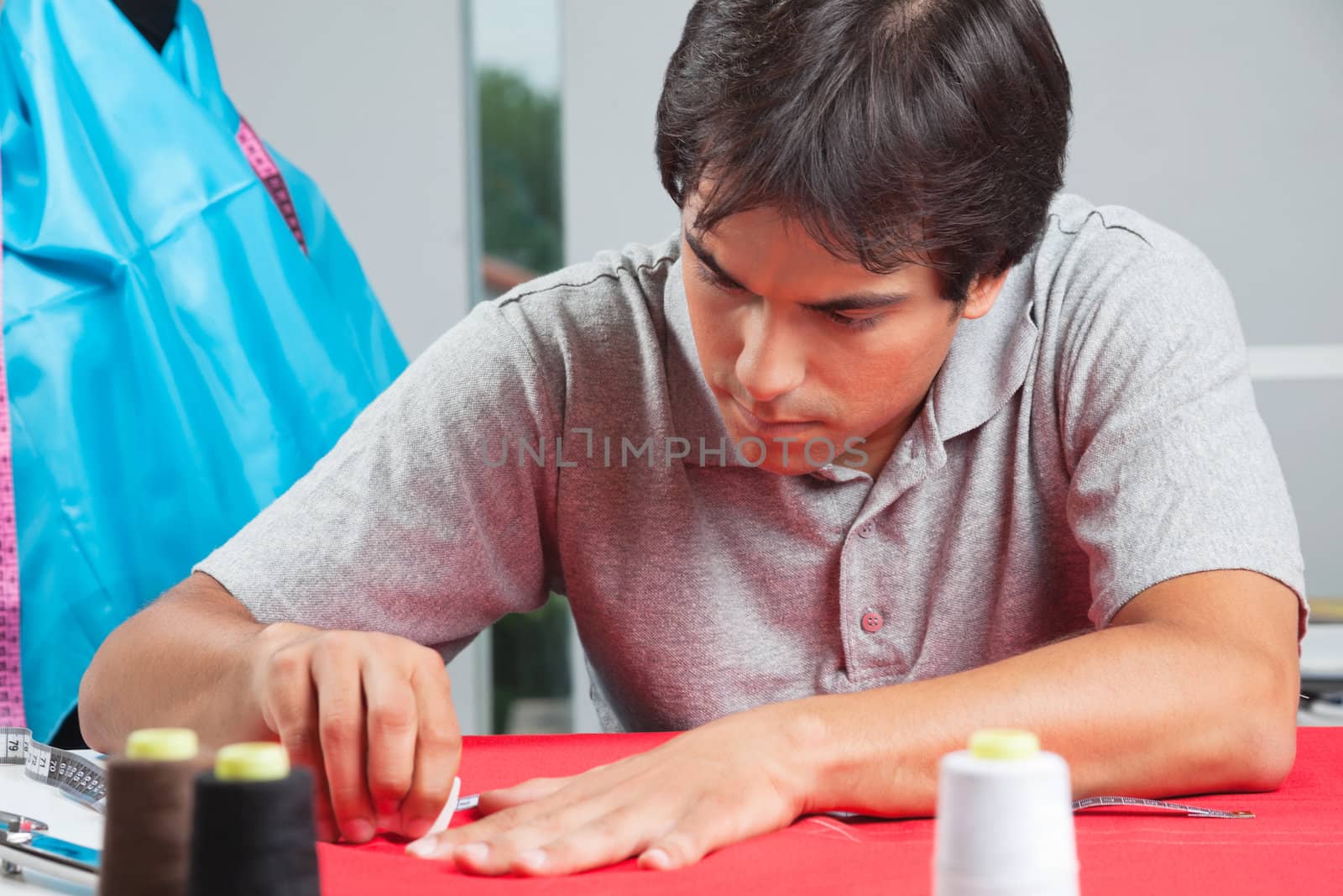 Young male dressmaker drawing line on a red fabric with chalk