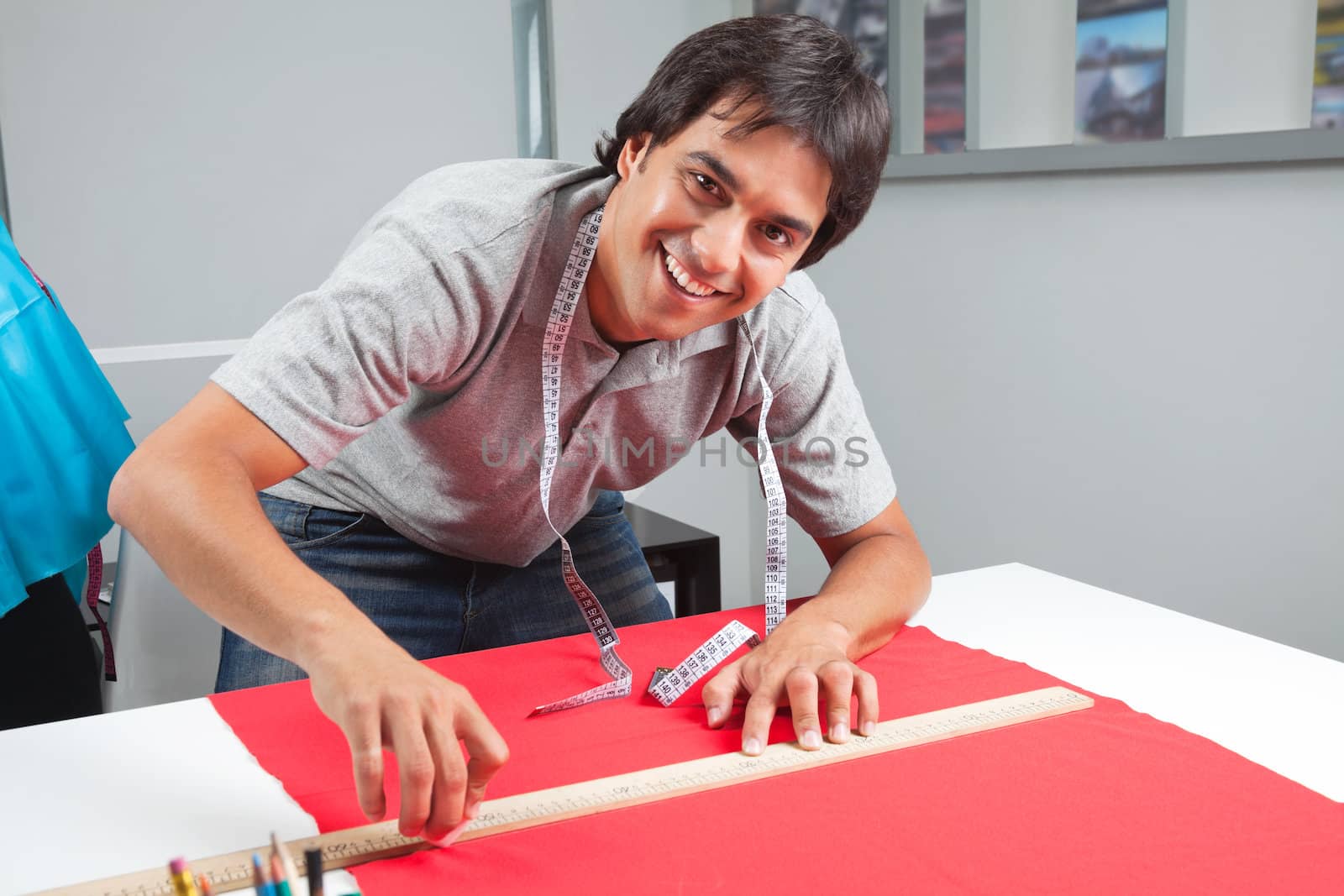 Portrait of young male dressmaker measuring a red fabric with ruler on table