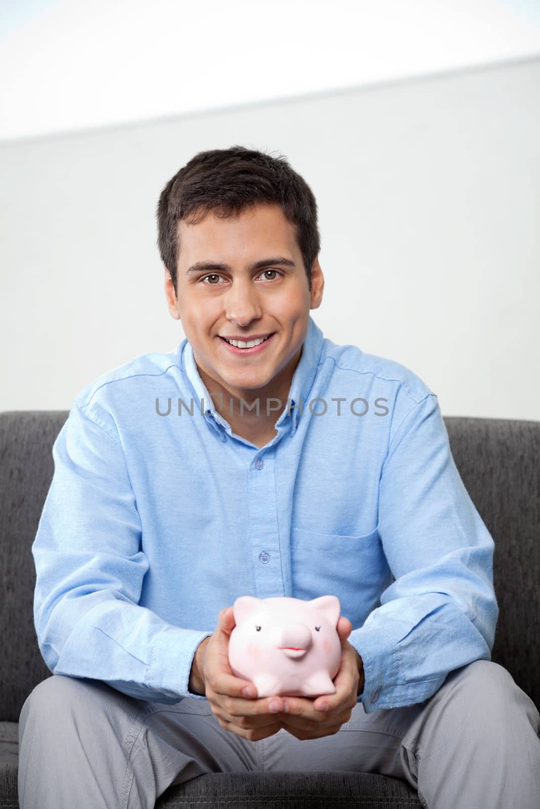 Portrait of handsome young businessman in formal wear holding piggybank