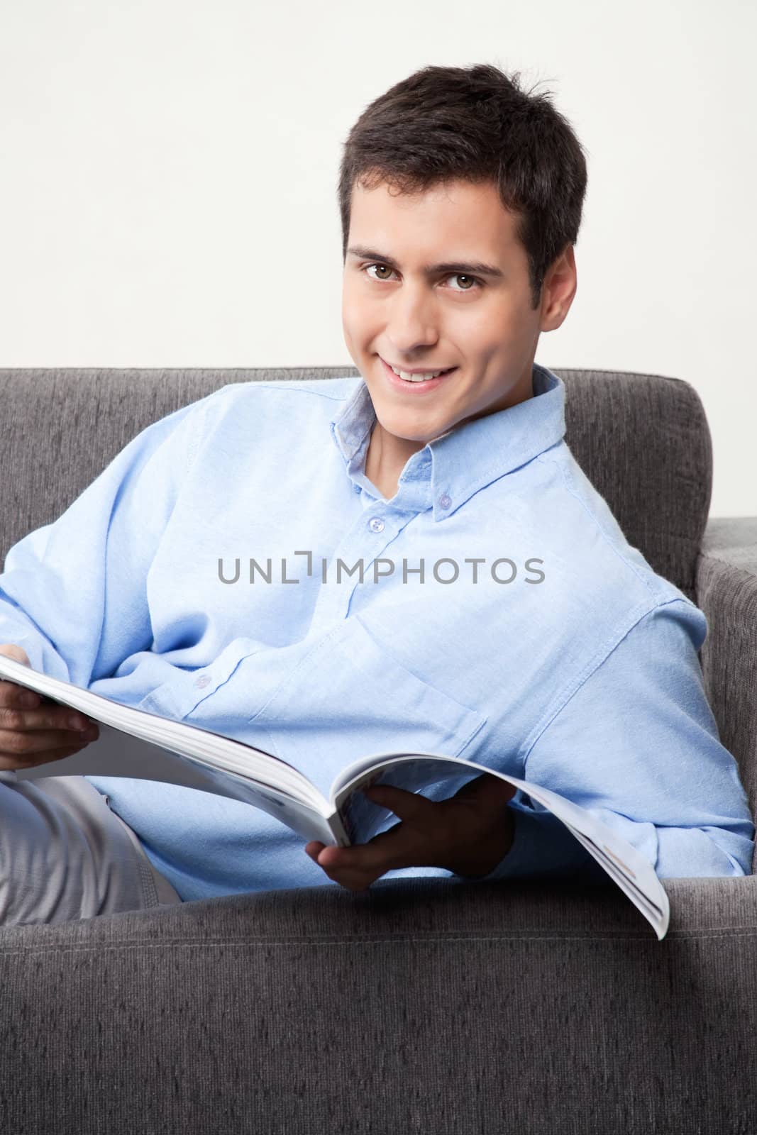 Young man holding magazine on couch.