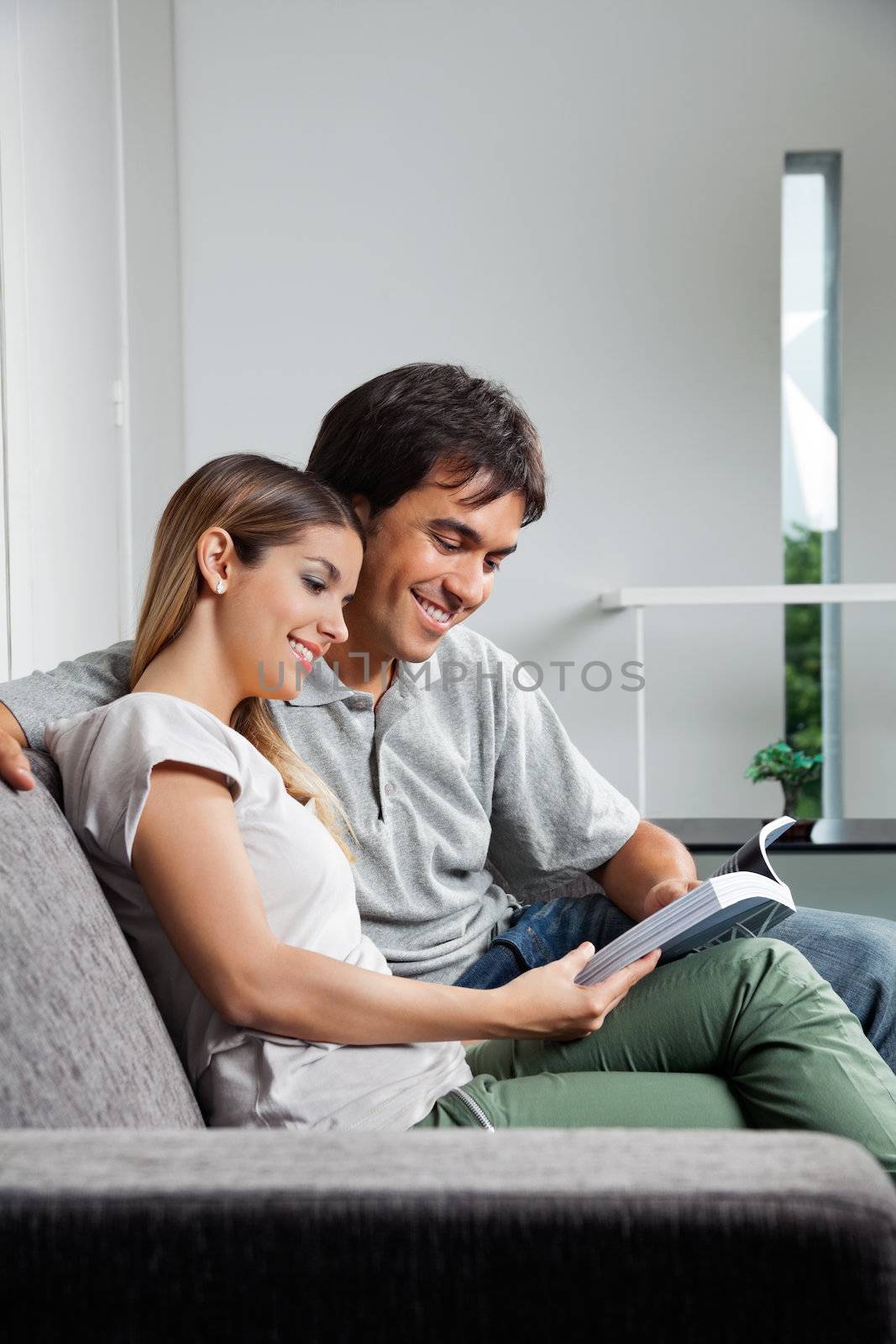 Young couple reading a book together while sitting on sofa at home