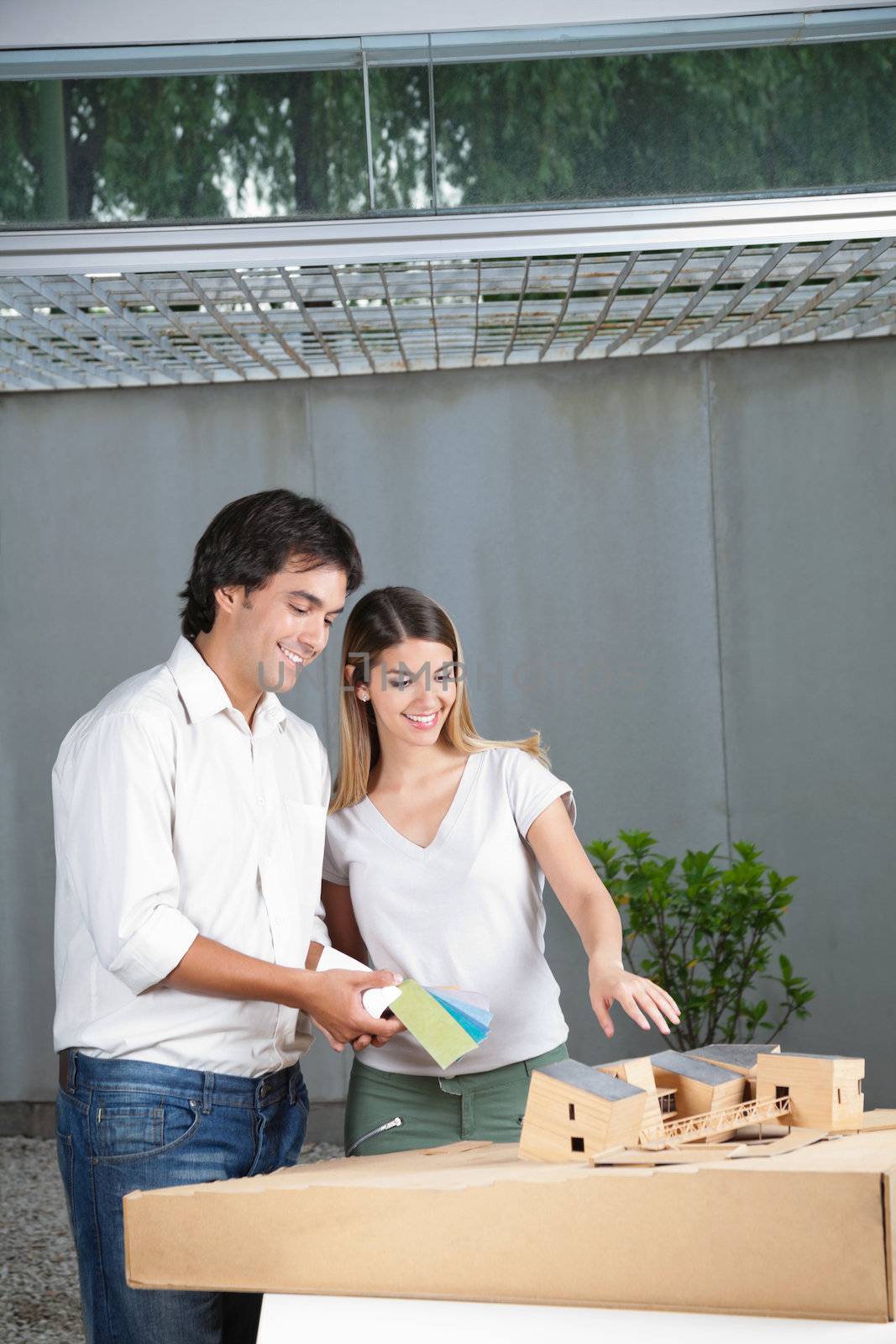 Female architect showing model house while colleague holds color swatches