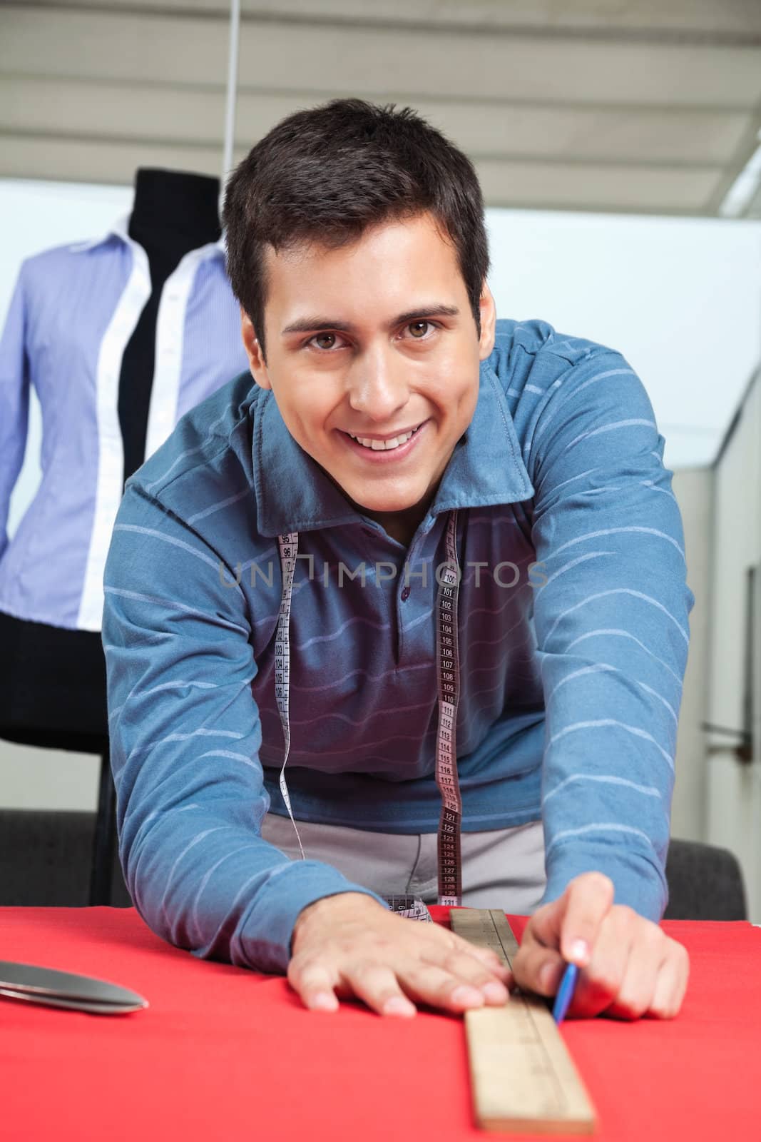 Portrait of happy young male tailor drawing line on a red fabric with chalk