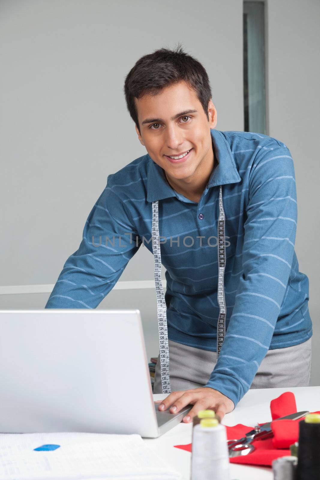 Portrait of young male tailor using laptop while standing by table