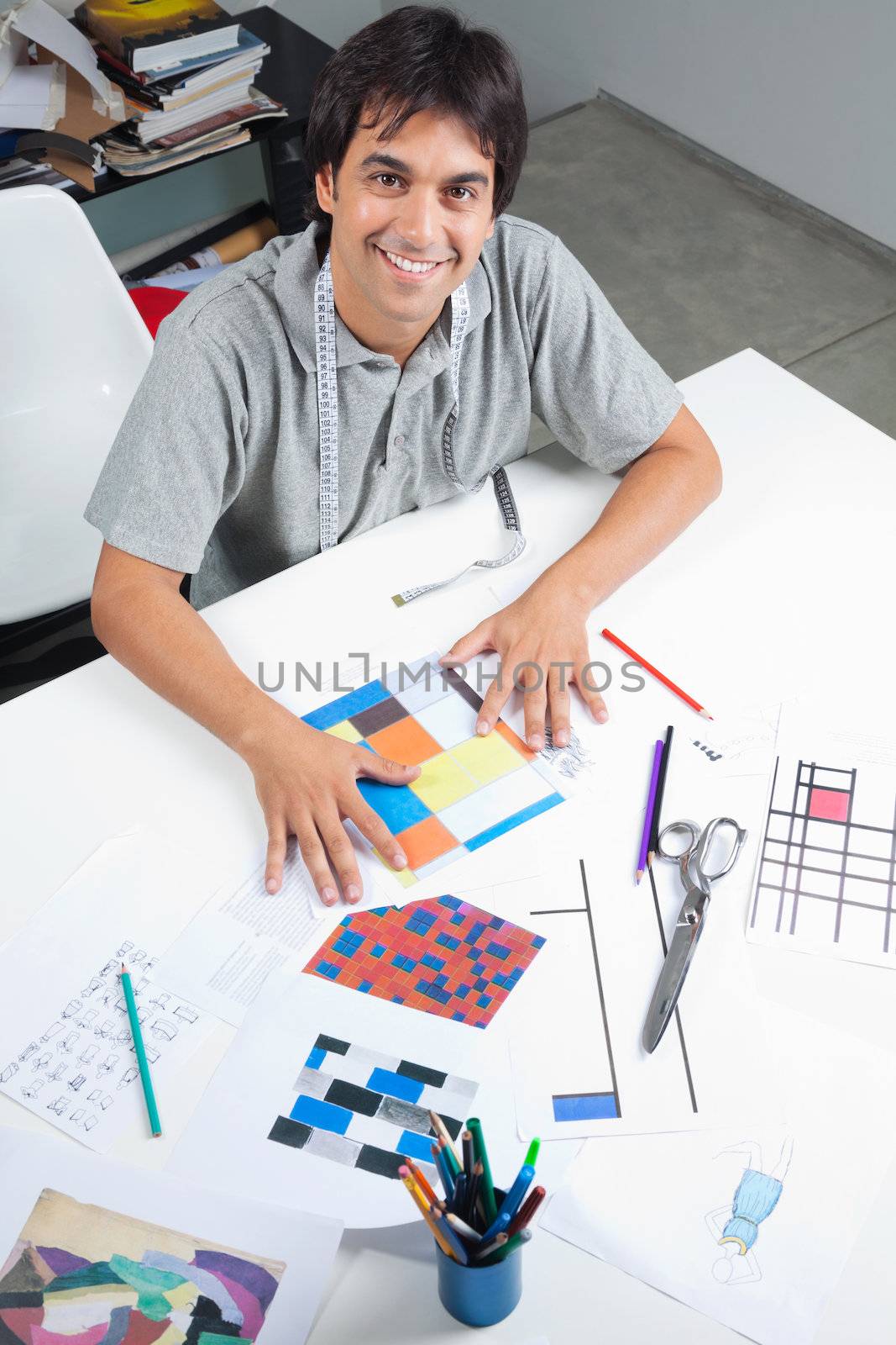High angle view of male fashion designer sitting at table with outline designs and patterns at workshop