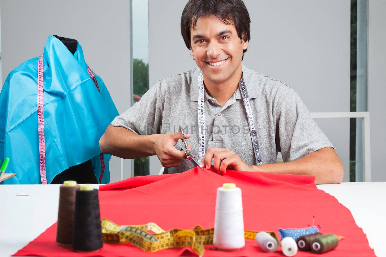 Portrait of young clothing dressmaker cutting red fabric with polyester threads on cloth