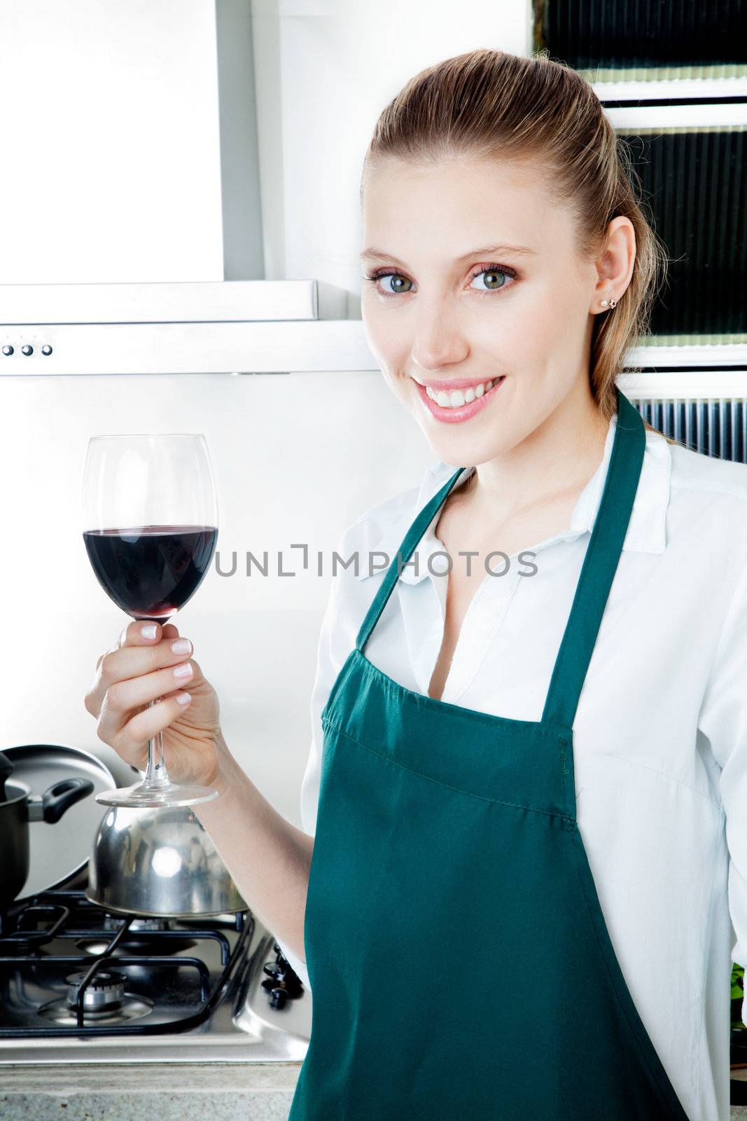 Pretty female blond woman in kitchen cooking with glass of red wine in hand