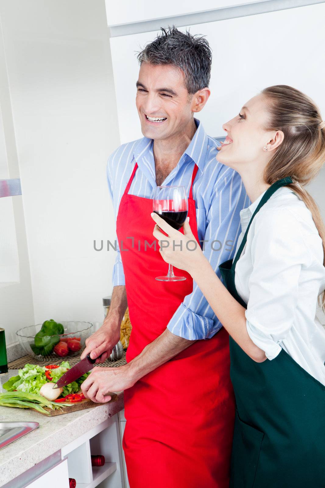 A happy laughing caucasian couple in the kitchen cooking food and drinking wine.