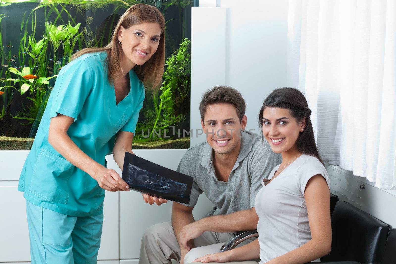 Portrait of a female dentist showing dental X-ray to young couple in clinic
