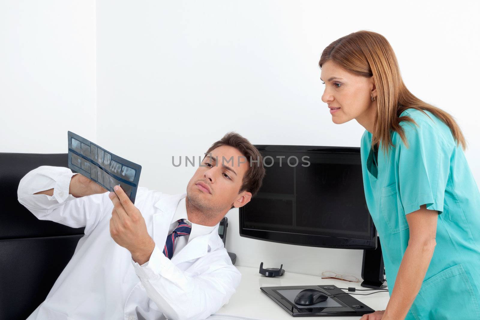 Male dentist and female assistant analyzing X-ray report at office desk