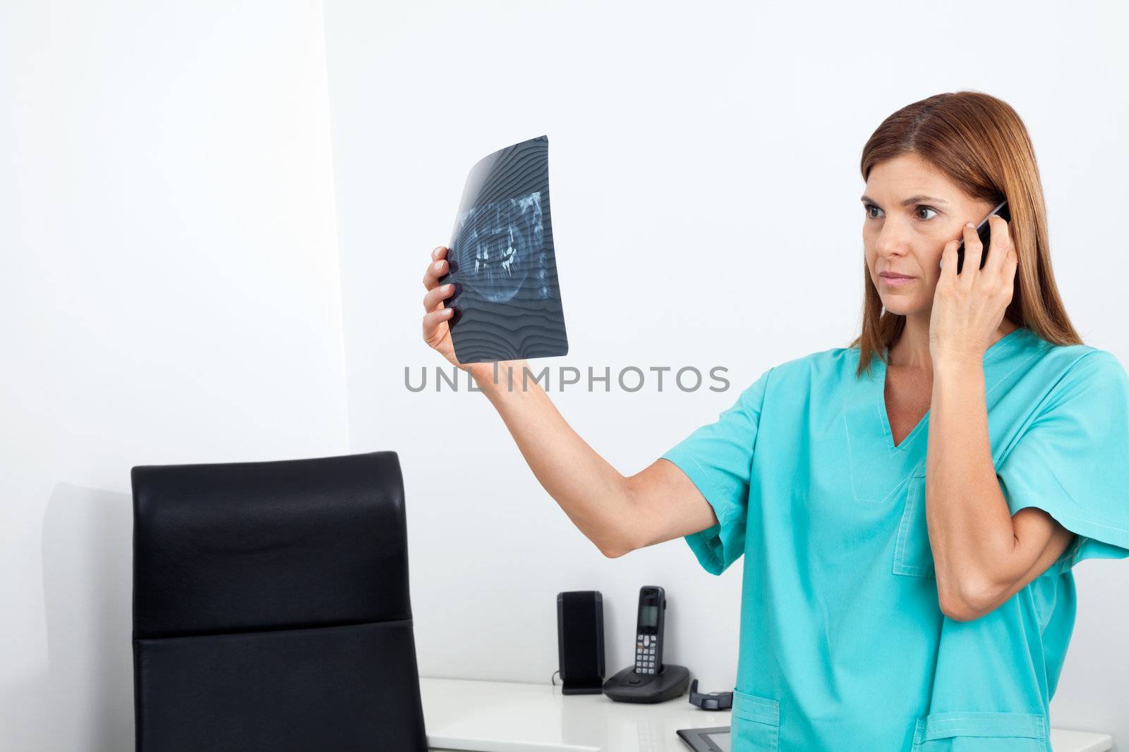Serious female dentist looking at X-ray report while using cellphone in clinic
