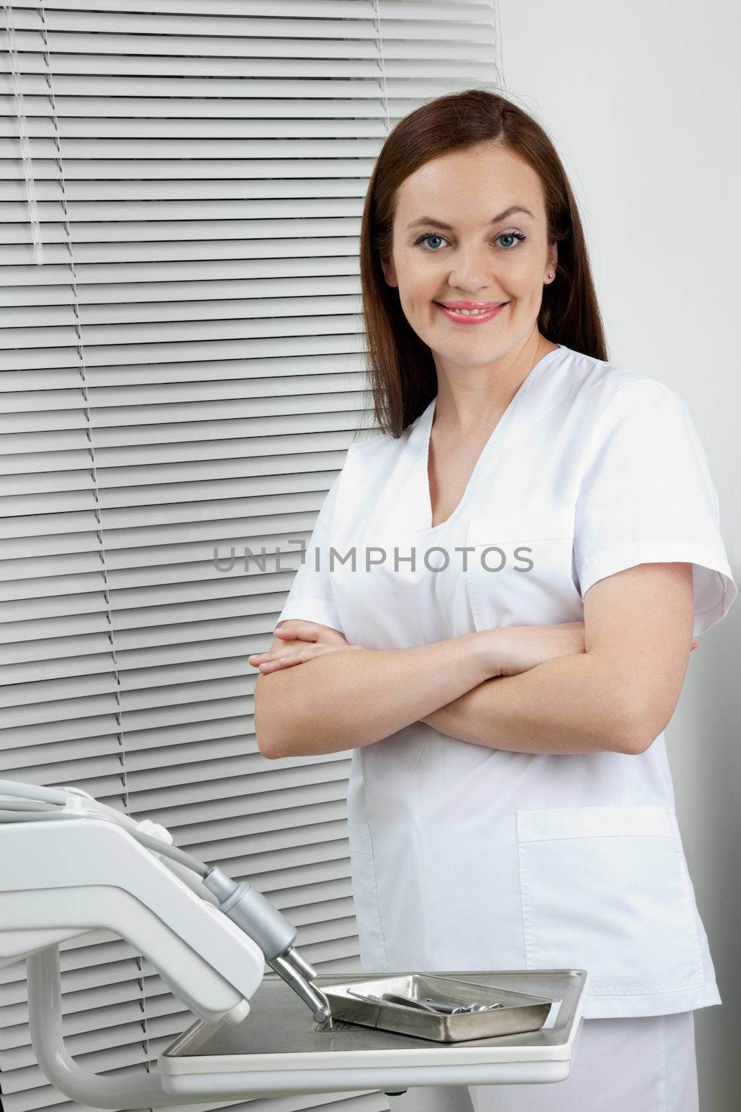 Portrait of happy confident female dentist standing with arms crossed in clinic