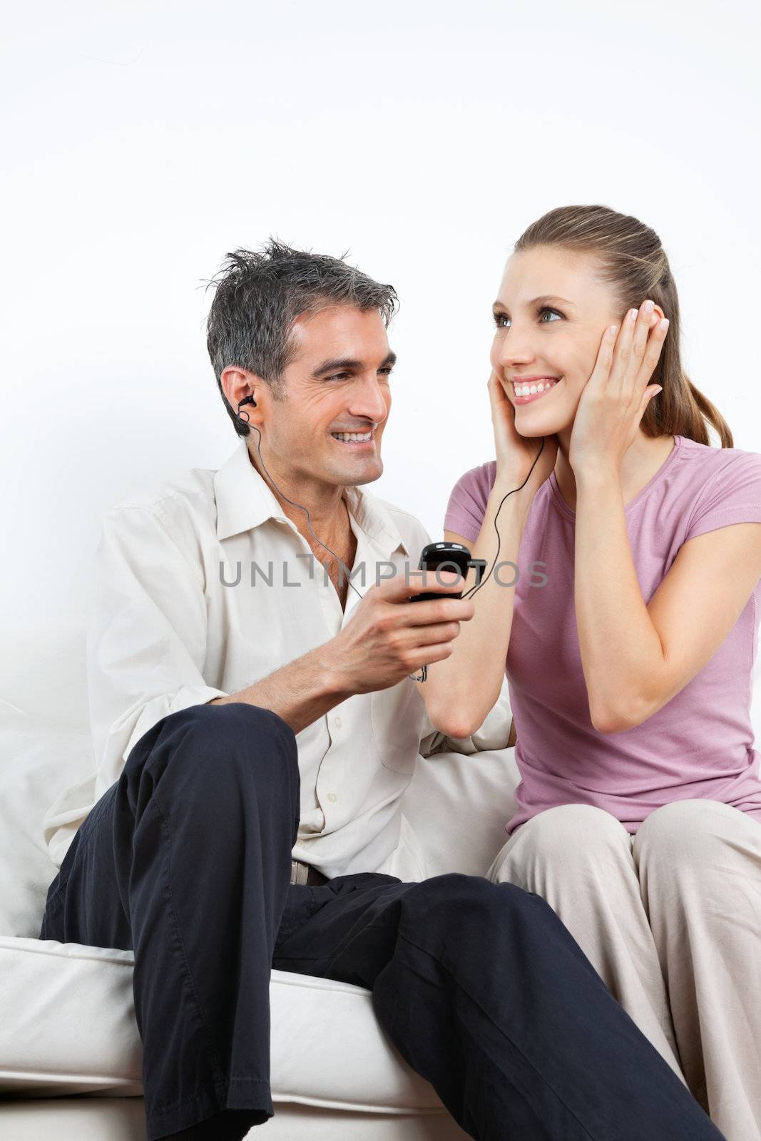 Happy couple listening music together on cell phone while sitting on sofa