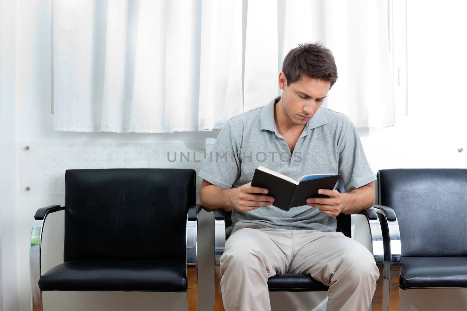 Young man reading book in doctor's waiting room