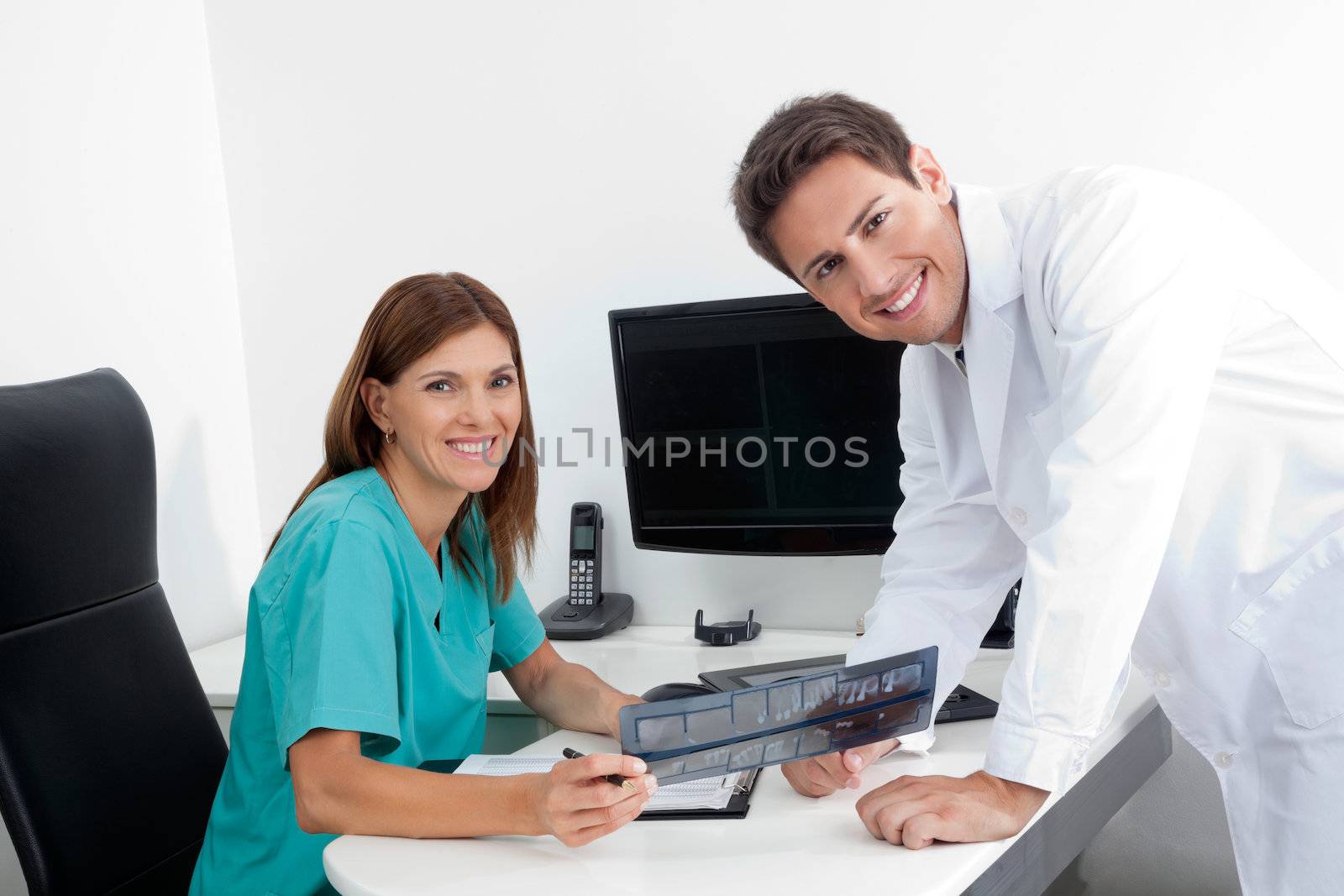 Portrait of happy dentist and female assistant analyzing X-ray report at office desk