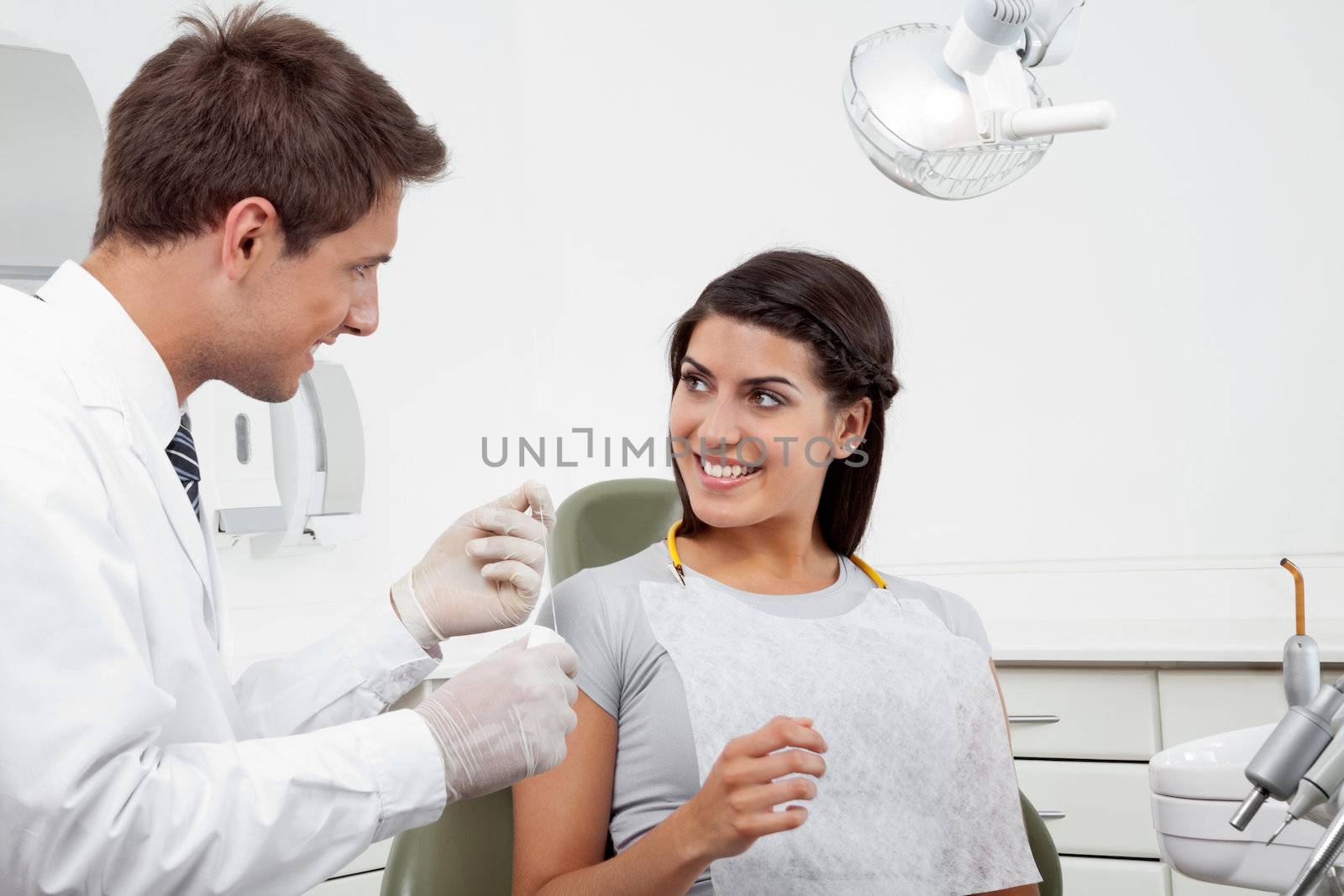 Happy young male dentist holding thread while patient looking at him in clinic
