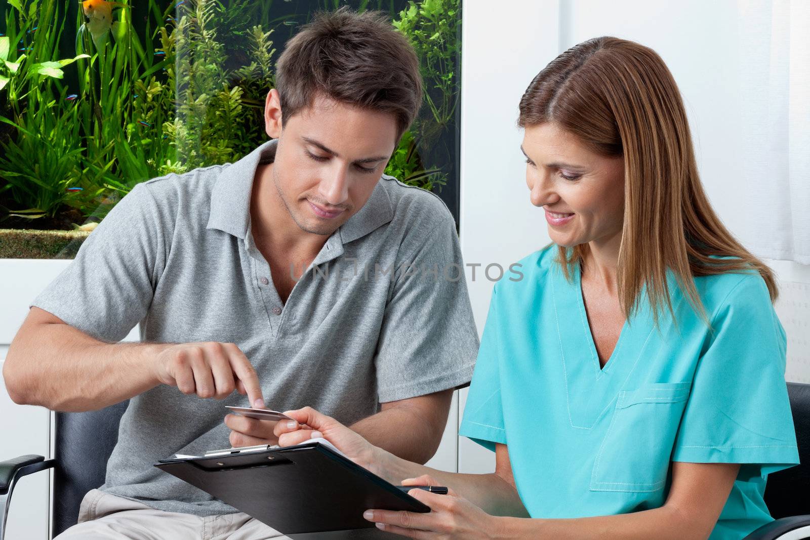 Young man paying bill through credit card to female dentist in clinic