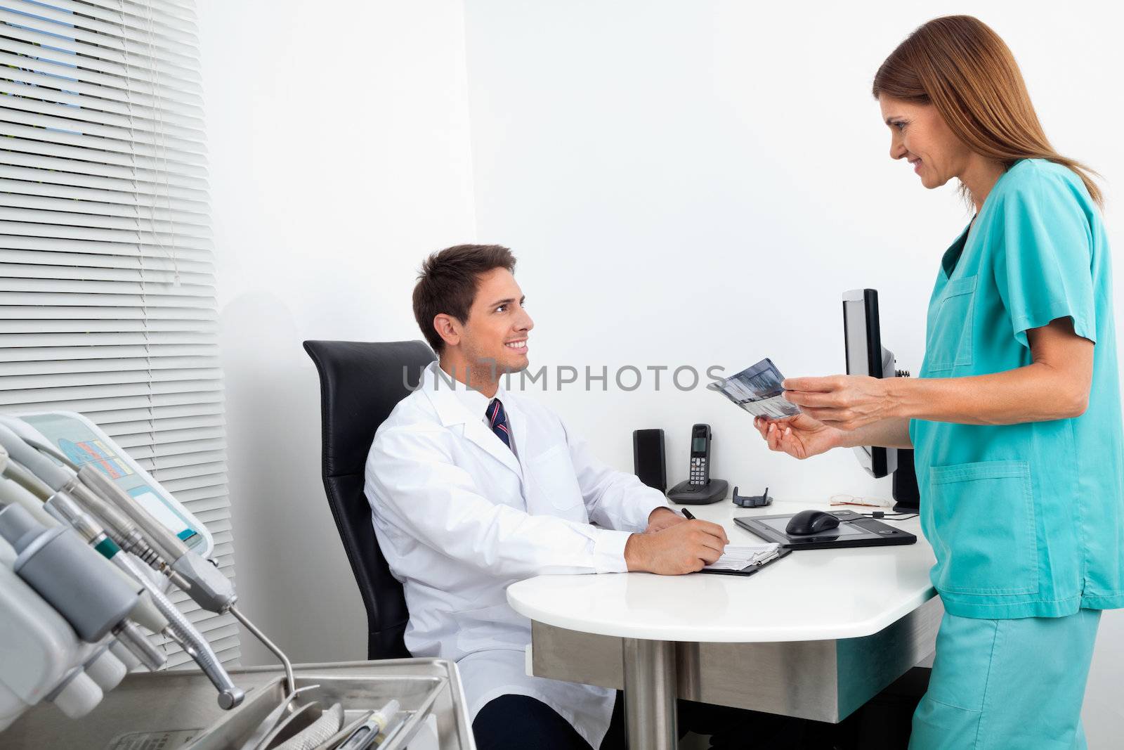 Male doctor with assistant holding X-ray report at office desk