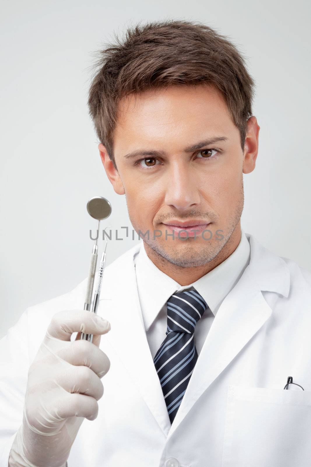 Portrait of young male dentist holding angled mirror and carver in clinic