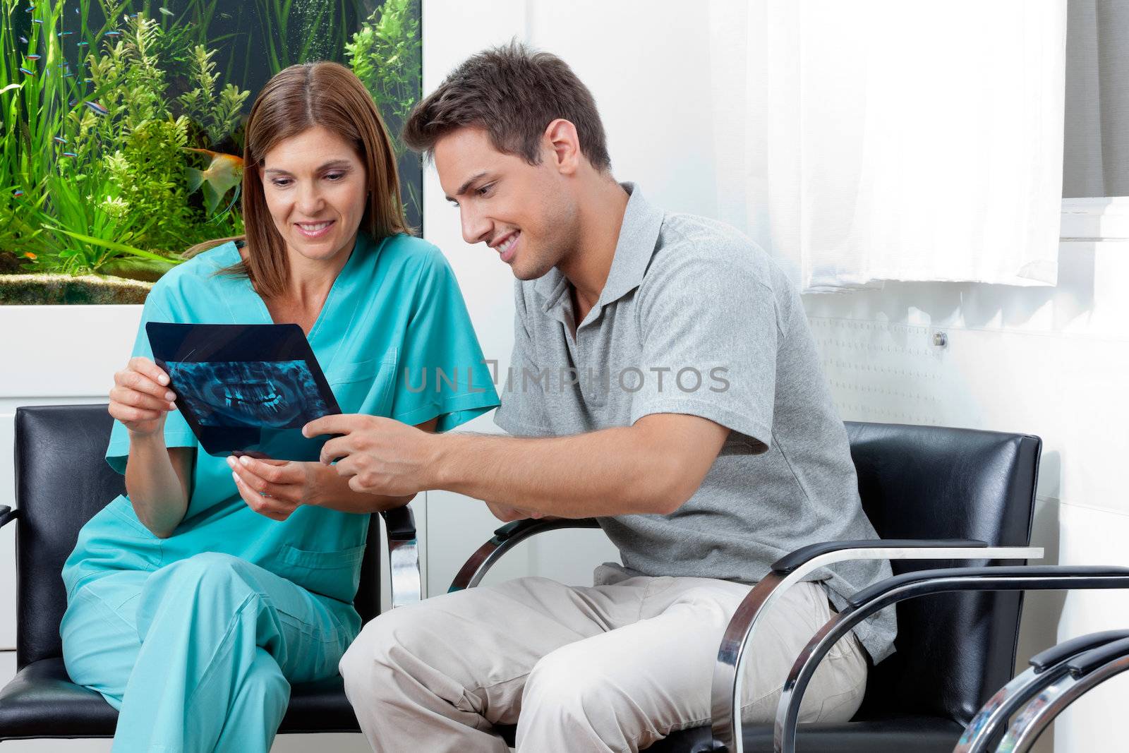 Female dentist showing dental X-ray report to young man in clinic