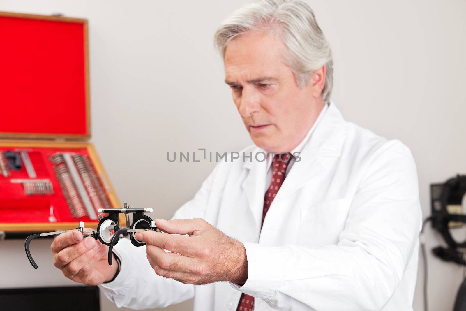 Mature optometrist examining trial frame for eye examination in the clinic