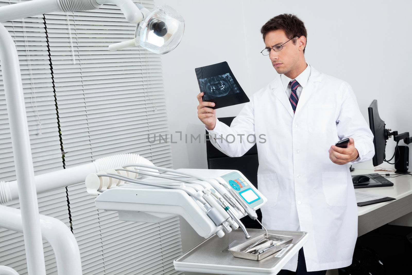 Male dentist analyzing patient's X-ray report in examination room