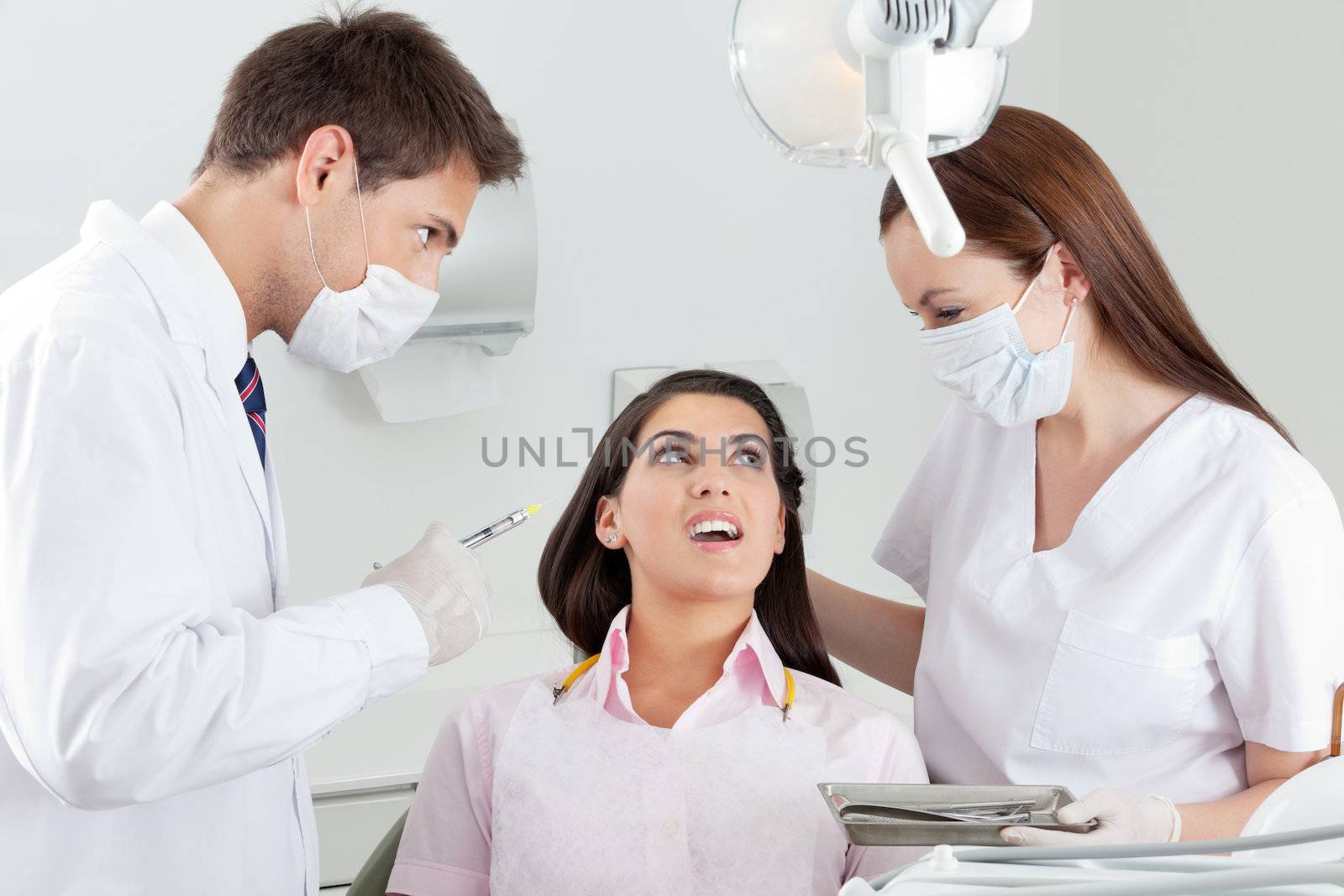 Young male dentist looking at nurse comforting patient in clinic