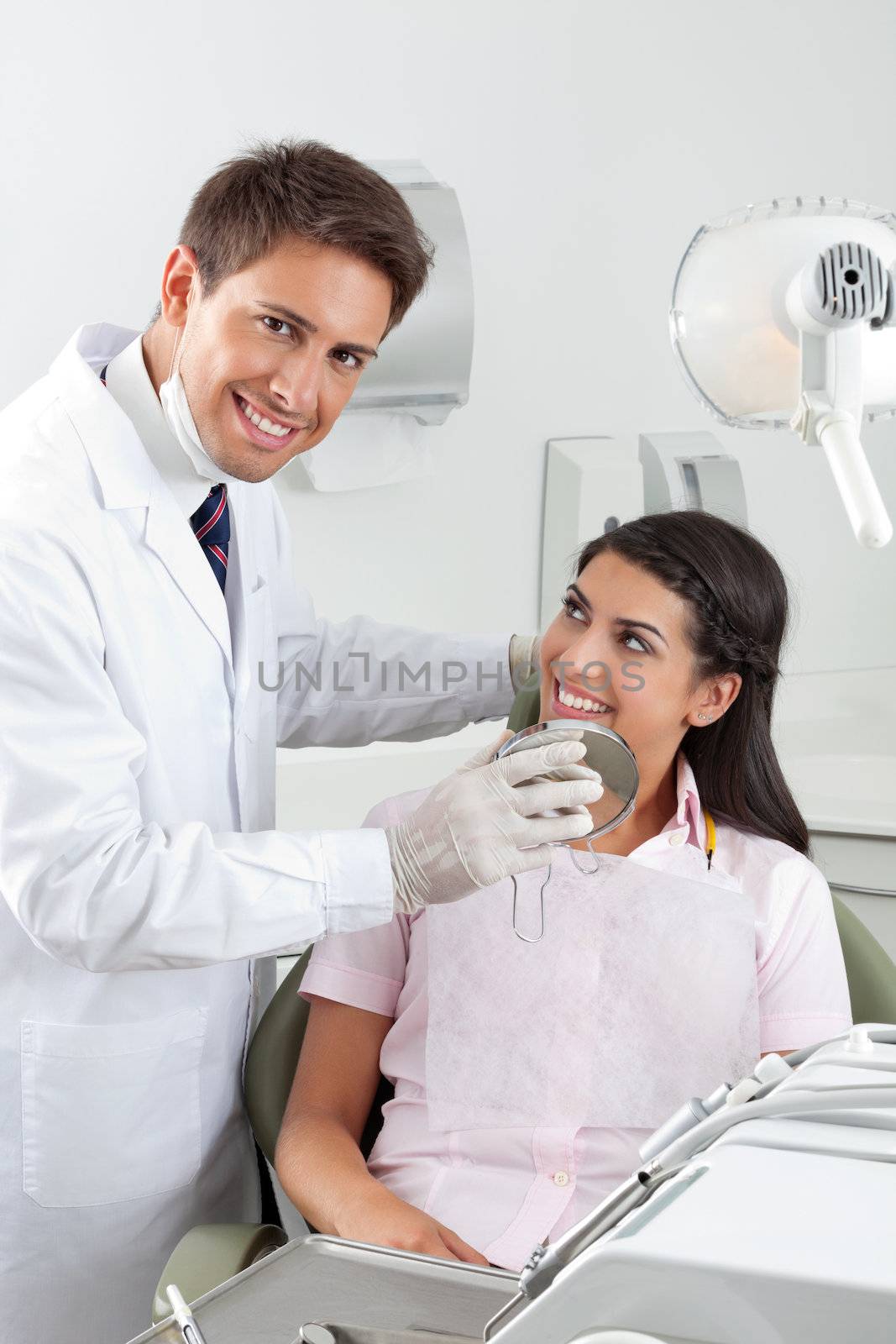 Portrait of happy young male dentist showing the result of his work to the satisfied patient