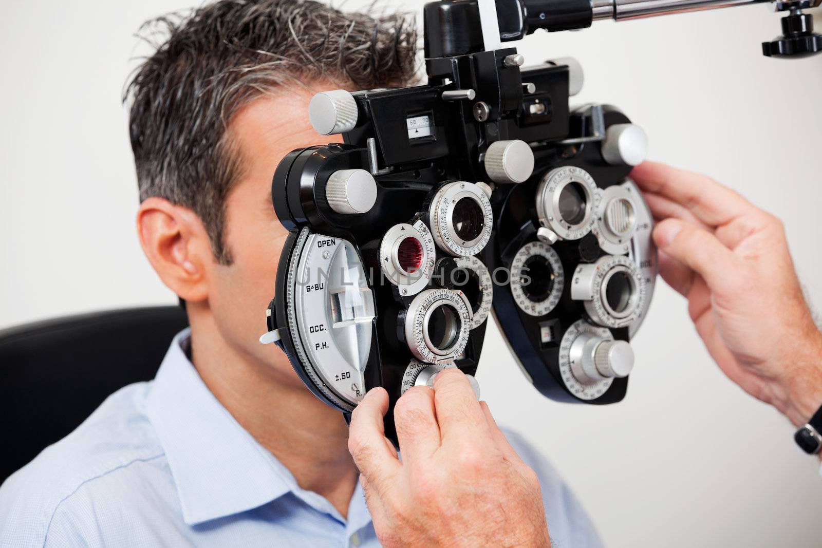 Optometrist adjusting panels of phoropter while examining his patient