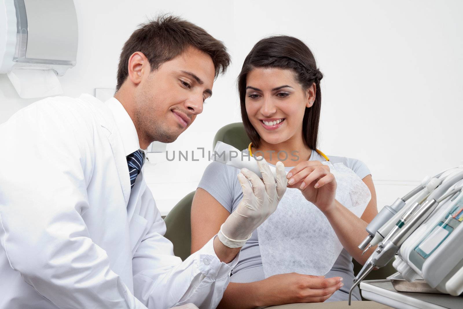 Happy young male dentist prescribing tooth paste to female patient in clinic