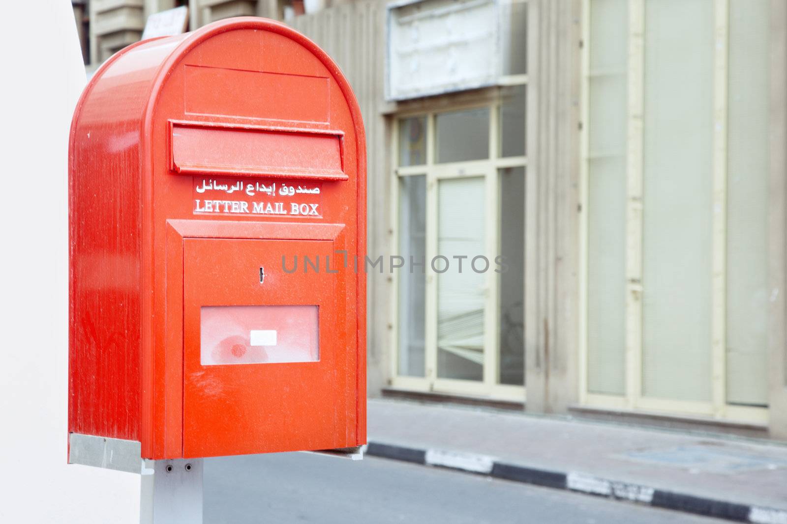 Red mail box outdoors with English and Arabian text