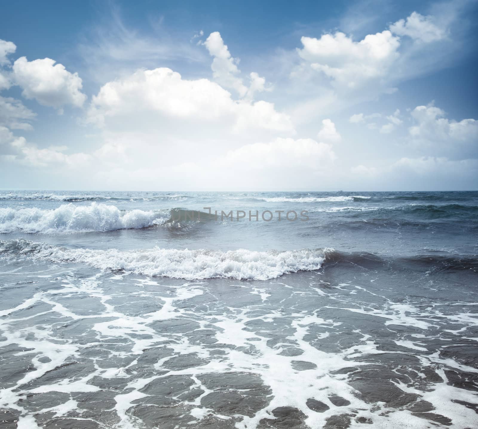 View on the blue sea with waves and spindrift under the cloudy sky