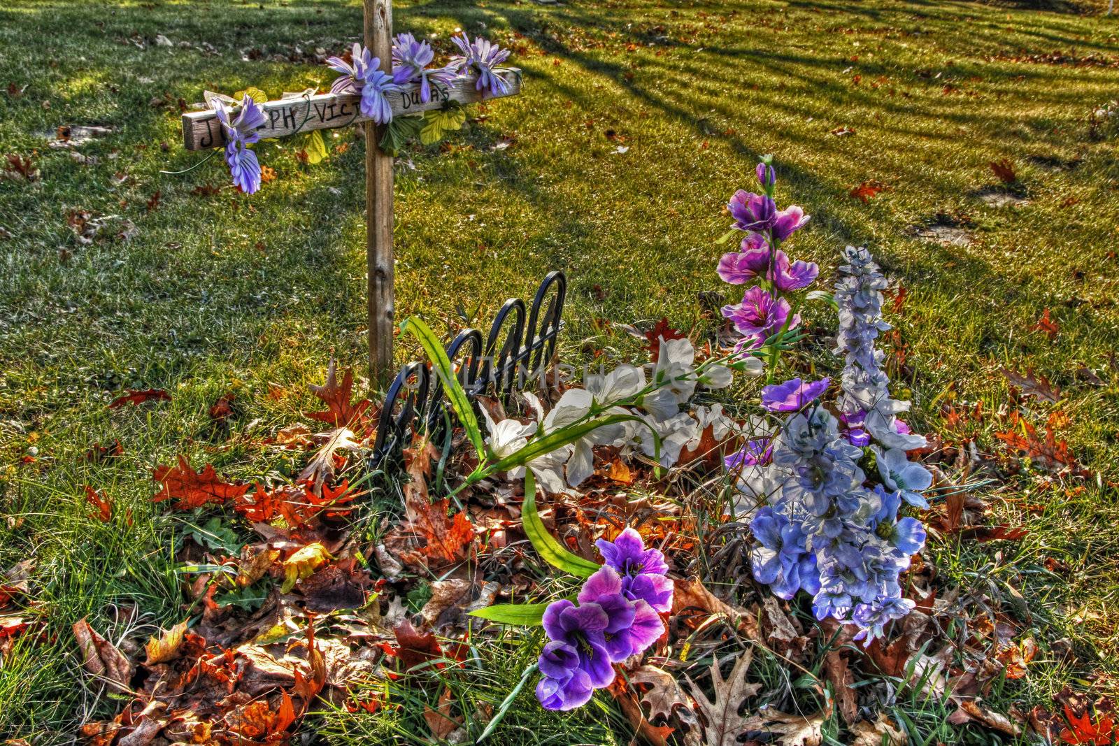 Wooden cross in graveyard covered with colorful flowers