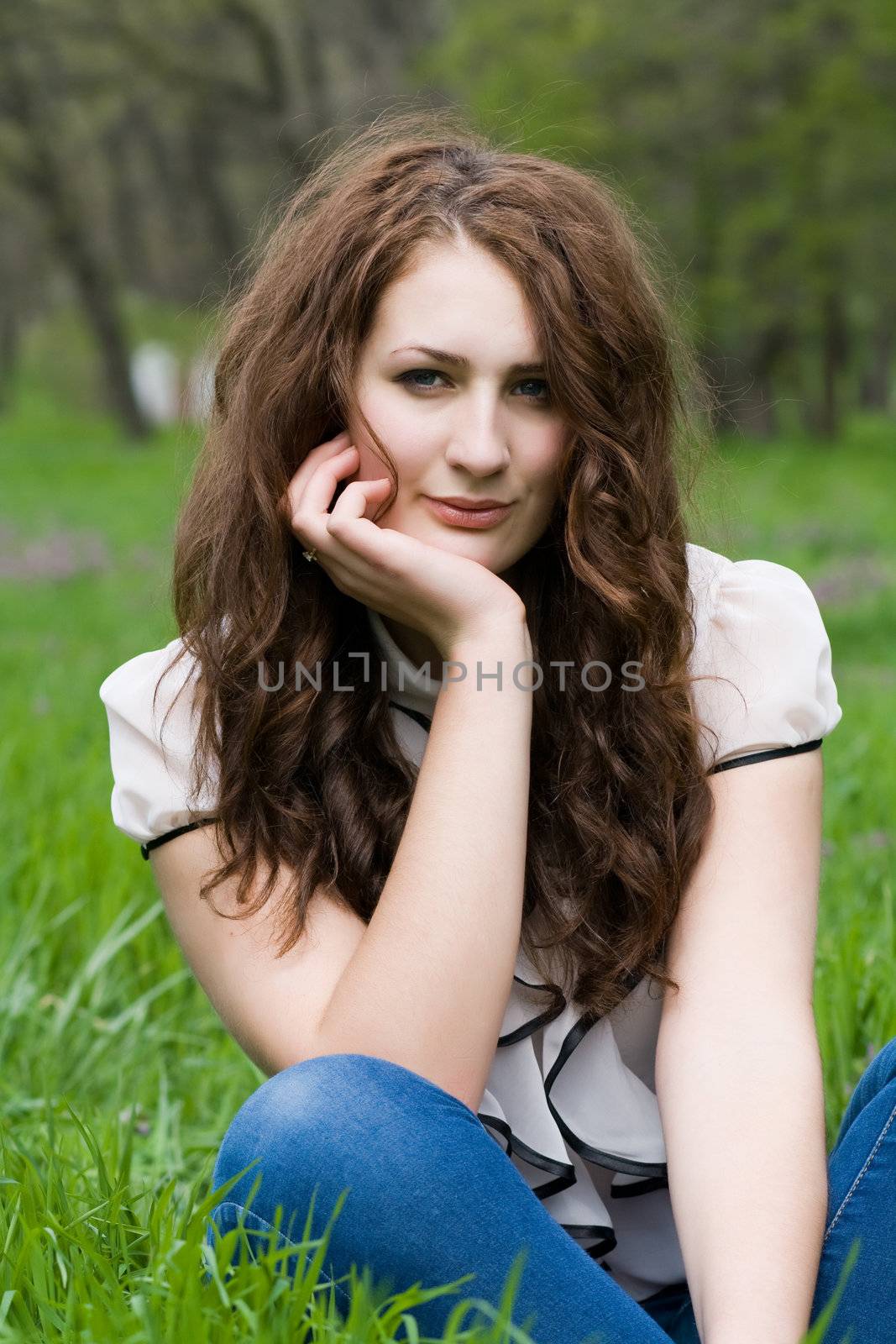 Beautiful and cute girl thoughtfully sitting on the green grass