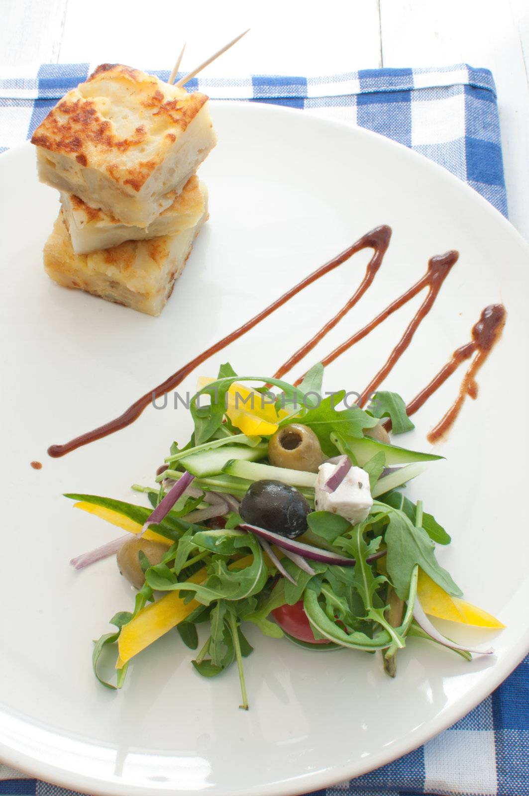 Healthy salad with cucumber and pepper on a plate with dressing and a potato omelette 