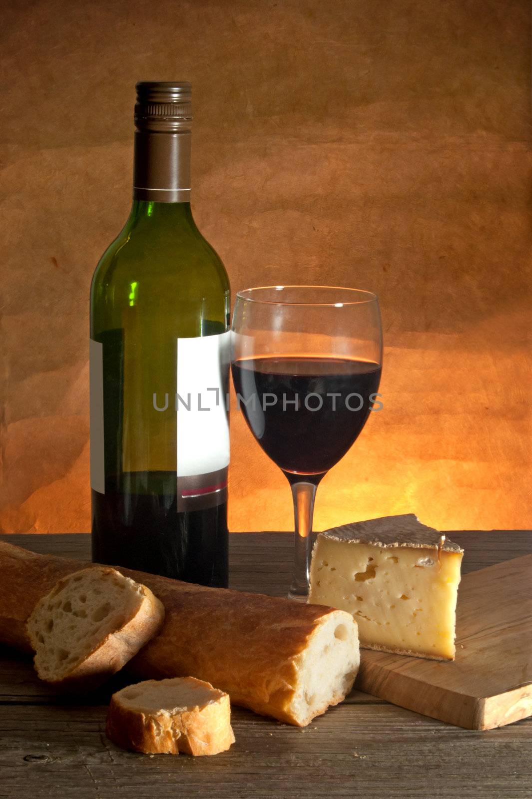Glass of red wine with cheese and a sliced loaf of freshly made french bread