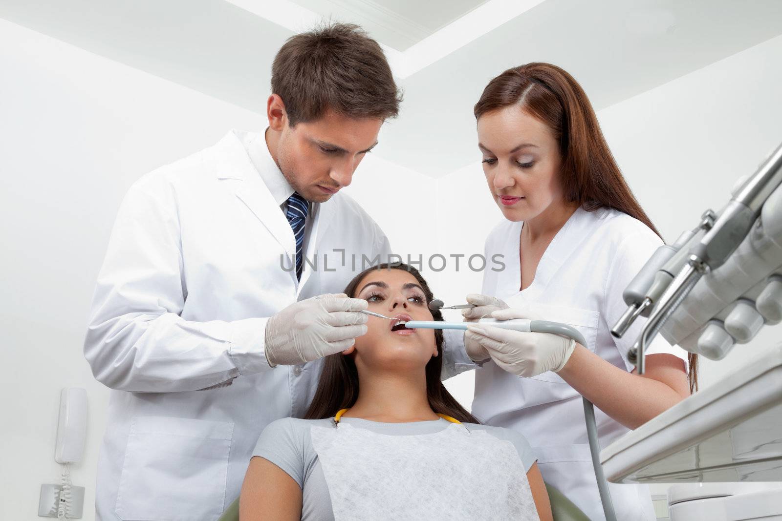 Young male dentist and nurse examining patient's teeth in clinic