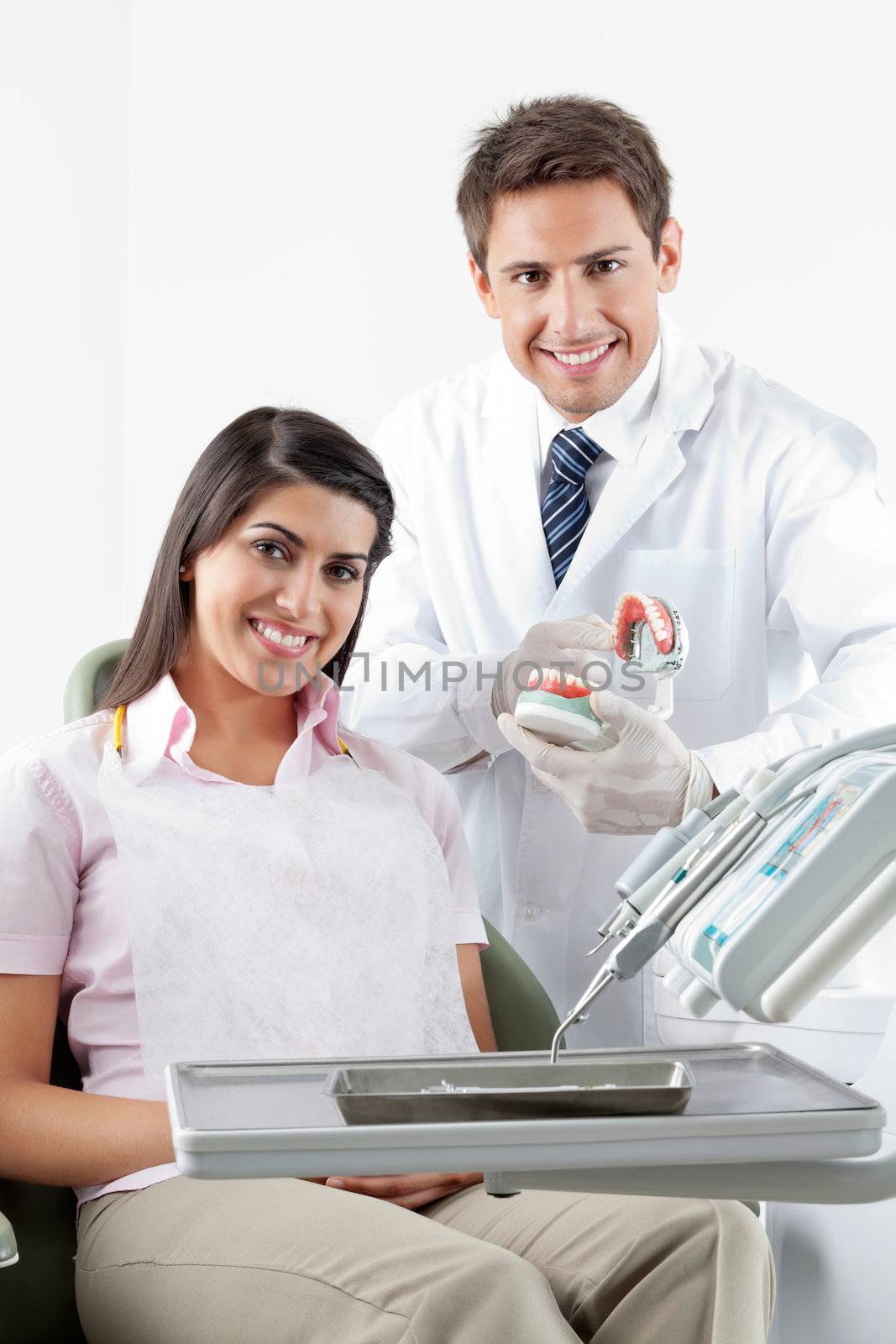 Portrait of happy male dentist and patient with teeth model in clinic
