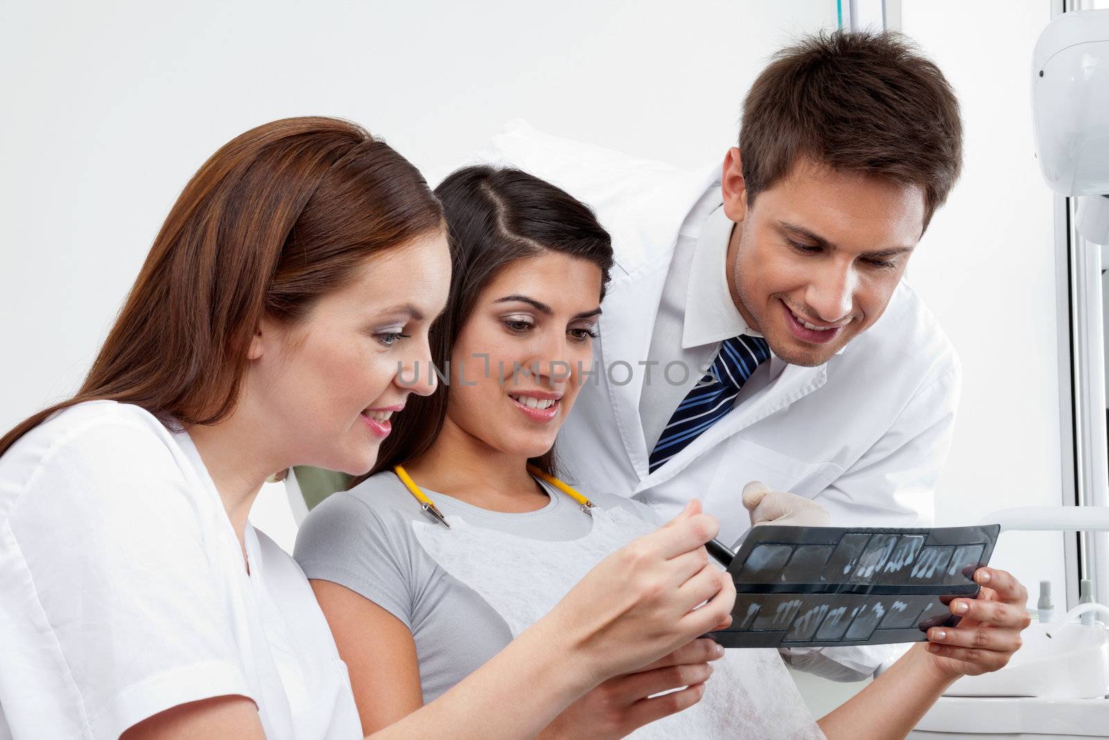 Female nurse and dentist explaining X-ray report to patient with doctor in the background