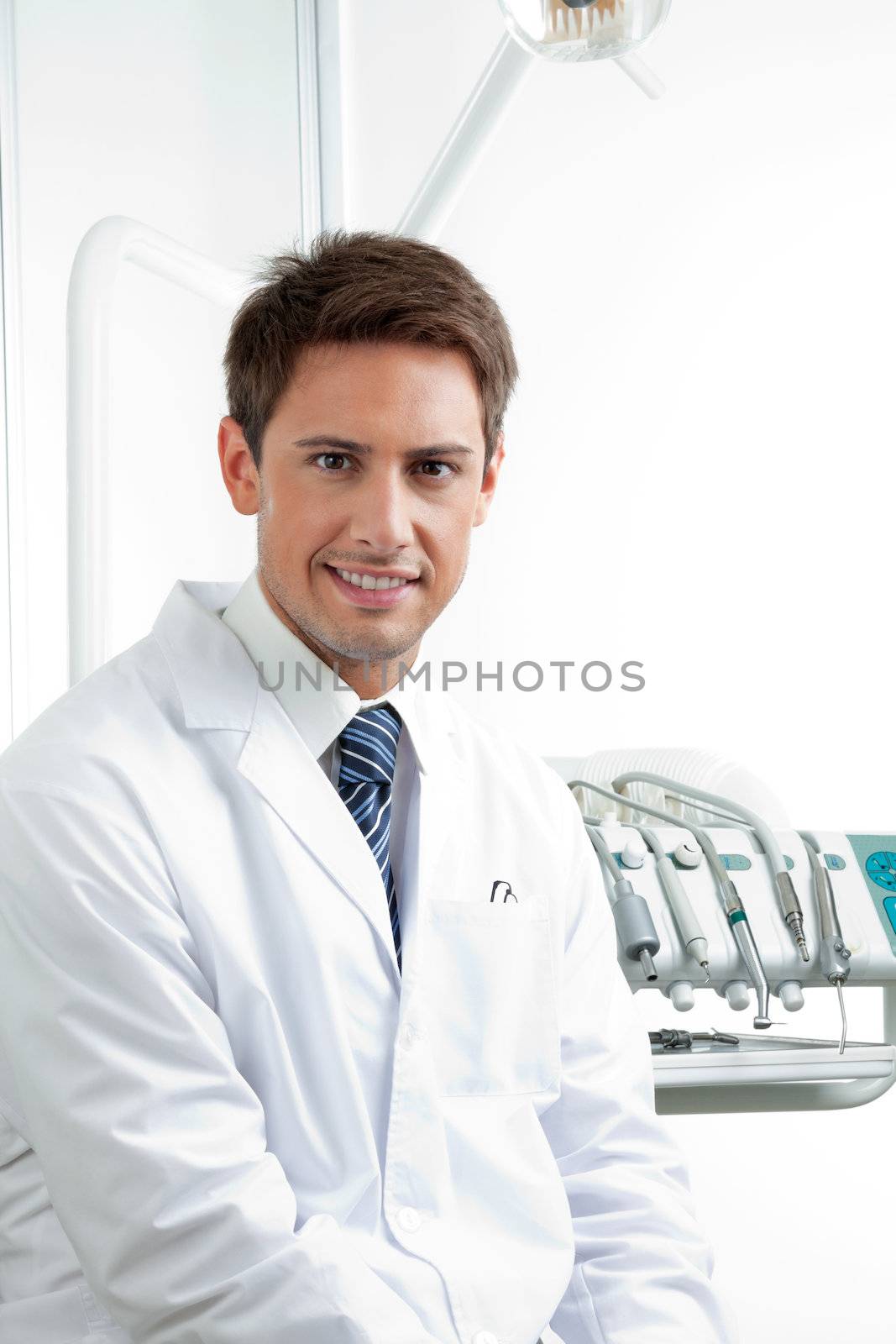Portrait of happy male dentist sitting in clinic
